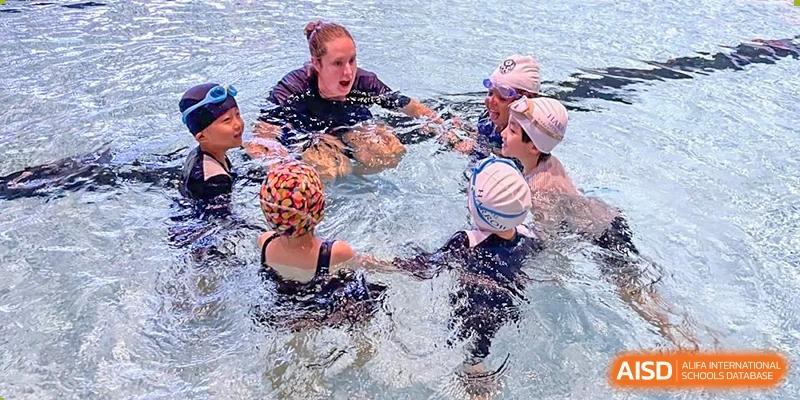 Harrow International School Shenzhen students in a swimming lesson, gathered around an instructor in a pool.