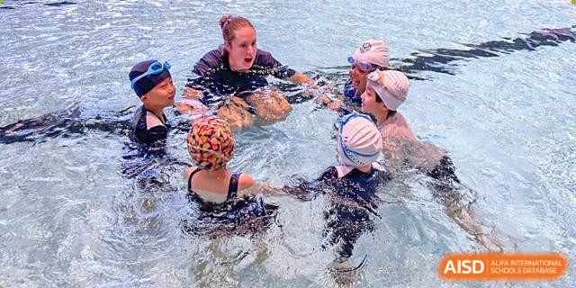 Harrow International School Shenzhen students in a swimming lesson, gathered around an instructor in a pool.