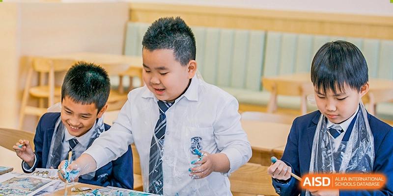 Harrow International School Shenzhen student in a school uniform, smiling and holding an item while seated at a desk.