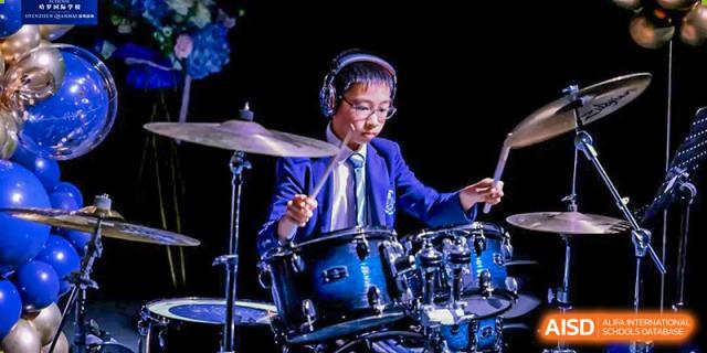 Harrow International School Shenzhen student wearing headphones and playing the drums during a musical performance.