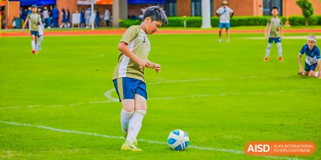 Harrow International School Shenzhen student's foot next to a soccer ball on a green field.