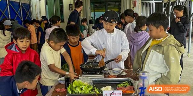 Harrow International School Shenzhen students cooking together in a kitchen class, with one student stirring a pan on a stove.
