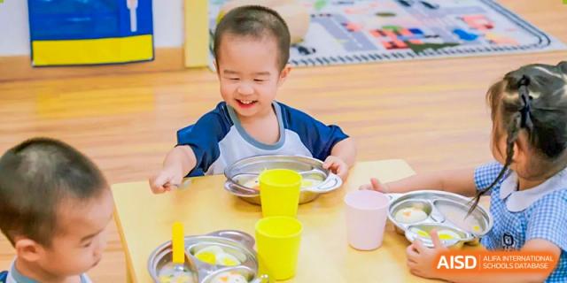 Harrow International School Shenzhen young student smiling while using a bowl and cup at a table.