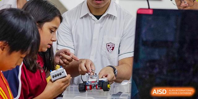 International School of Nanshan Shenzhen close-up of students working together on a small robot made of building blocks.