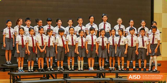 International School of Nanshan Shenzhen young students in school uniforms standing on risers, possibly for a choir or performance.