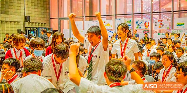 International School of Nanshan Shenzhen students cheering enthusiastically with their hands in the air during an event.