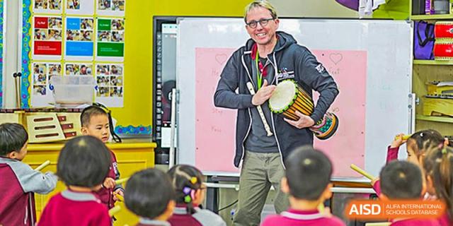 International School of Nanshan Shenzhen teacher playing a djembe drum in front of a group of young students.