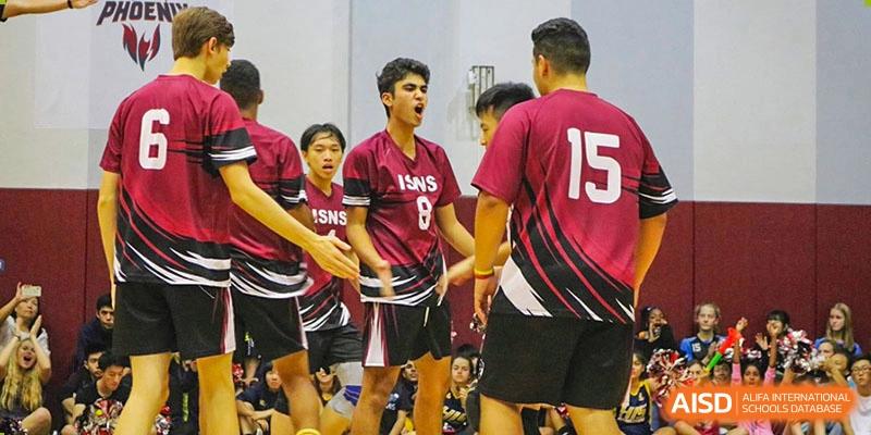International School of Nanshan Shenzhen boys' volleyball team in maroon uniforms celebrating or huddling together during a game.
