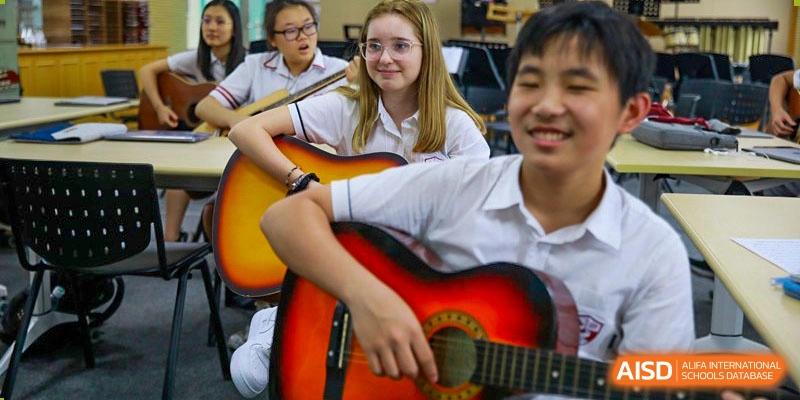 International School of Nanshan Shenzhen a male student playing an acoustic guitar while a female student smiles and watches him.