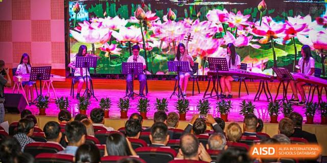 International School of Nanshan Shenzhen students performing on stage with traditional instruments in front of an audience.