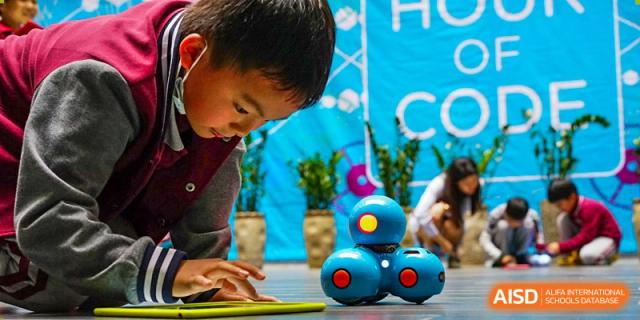International School of Nanshan Shenzhen student programming or interacting with two small blue robots.