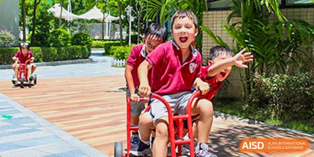 International School of Nanshan Shenzhen young student smiling and riding a small red scooter on school grounds.
