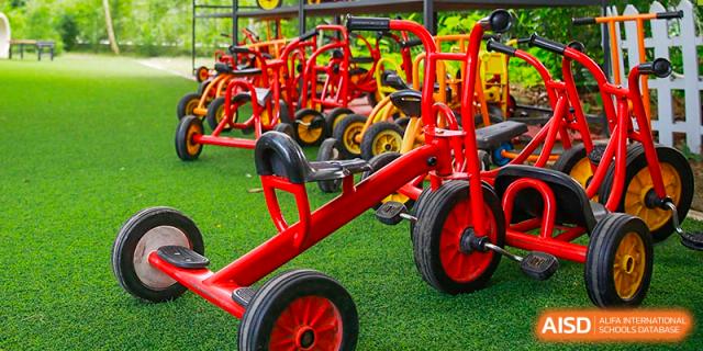 International School of Nanshan Shenzhen playground with several red and yellow riding toys on artificial grass.