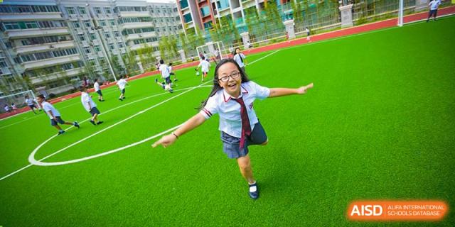 International School of Nanshan Shenzhen smiling female student running and playing on a grassy field.