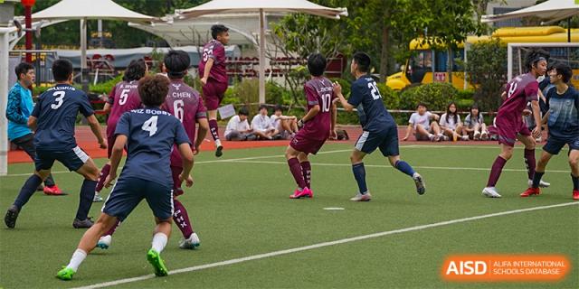International School of Nanshan Shenzhen boys' soccer team playing a game on a green field.