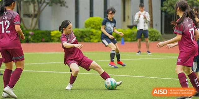 International School of Nanshan Shenzhen female student in a maroon uniform kicking a soccer ball during a match.