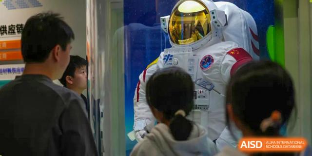 A Shenzhen Yunding School student views a display related to space or an astronaut simulation, facing away from the camera.