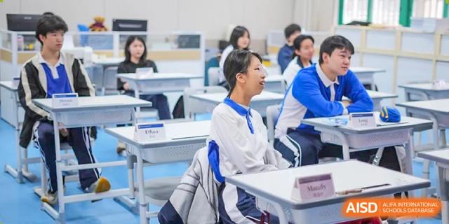 Two smiling Shenzhen Yunding School students sitting at their desks in a brightly lit classroom.