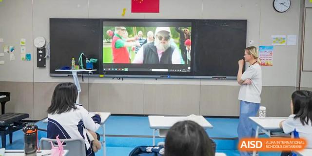 Shenzhen Yunding School students watching an educational video or lecture on a large television screen.