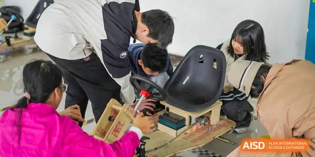 Shenzhen Yunding School students collaboratively working on a mechanical project, possibly a small vehicle or go-kart, adjusting components near the steering wheel.
