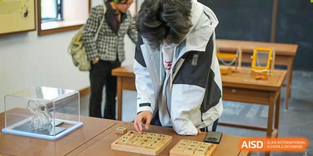 A Shenzhen Yunding School student focuses on playing a traditional wooden board game, possibly Go or a similar strategy game.