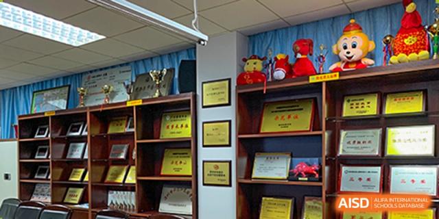 A wall display at Shenzhen Yunding School featuring various framed awards, certificates, and trophies.