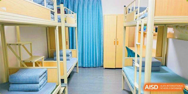 A clean and tidy dormitory room with yellow metal bunk beds and light blue curtains at Shenzhen Yunding School.