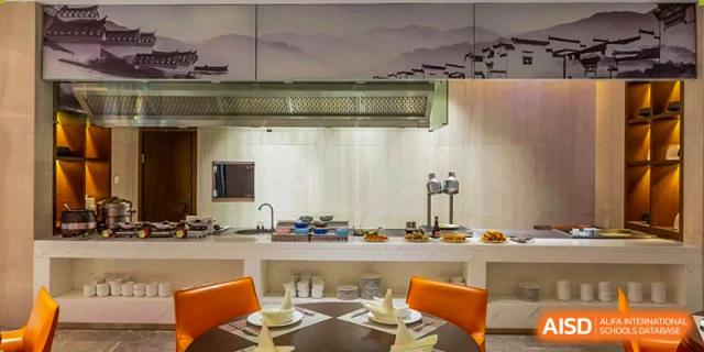 A modern, clean kitchen and dining area with orange chairs and a mountain-mural backdrop at Shenzhen Yunding School.
