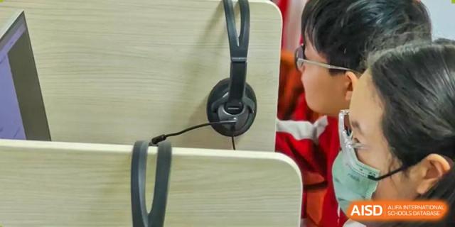 A student from Beijing Concord College of Sino-Canada is wearing headphones and looking at a computer screen during a class.