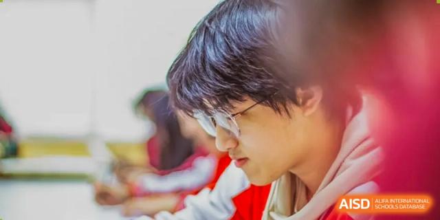 A student from Beijing Concord College of Sino-Canada is smiling and looking at another student in a classroom.