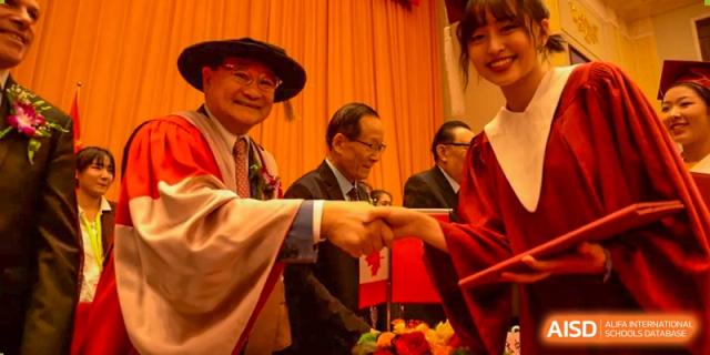 A man and a woman, possibly teachers or administrators from Beijing Concord College of Sino-Canada, are dressed in traditional Chinese attire, smiling and holding a red envelope.