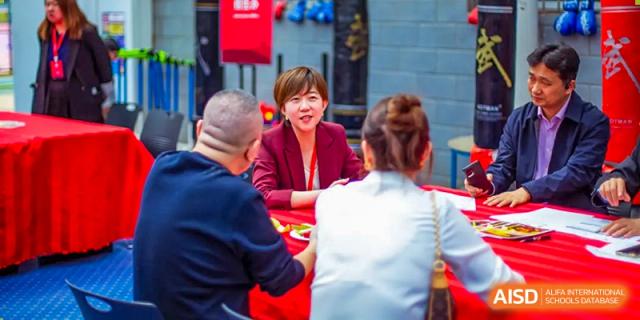 A group of adults, possibly parents and teachers from Beijing Concord College of Sino-Canada, are sitting around a table having a discussion.
