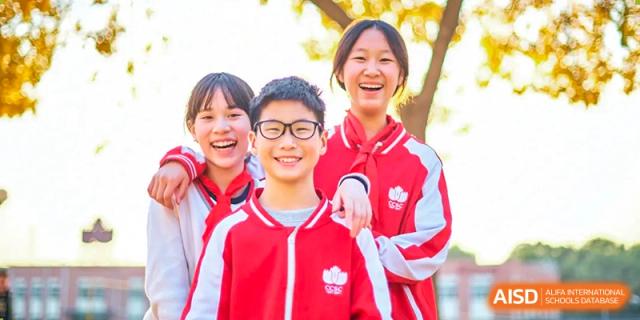 Three male students from Beijing Concord College of Sino-Canada, wearing red and white jackets, are smiling for a photo outdoors.