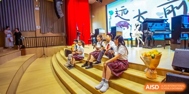 Students from Beijing Concord College of Sino-Canada are sitting on a stage with musical instruments, attending a school performance or concert.