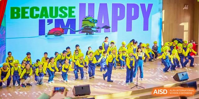 A group of students from Beijing Concord College of Sino-Canada is performing a dance or musical number on stage, all wearing matching yellow outfits.
