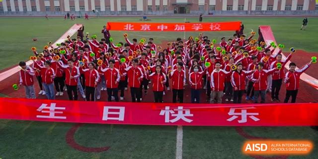 A large group of students from Beijing Concord College of Sino-Canada, all wearing matching red uniforms, stands in formation on a sports field under a banner.