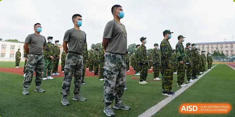 Students from Beijing Concord College of Sino-Canada, wearing military-style uniforms and masks, stand in a line during a school event or training.
