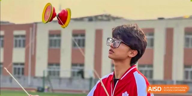A male student from Beijing Concord College of Sino-Canada is looking up and playing with a Chinese diabolo on a sports field.