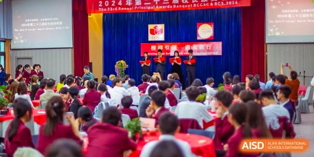 Students from Beijing Concord College of Sino-Canada are seated in an auditorium, watching a performance on stage with a red backdrop.