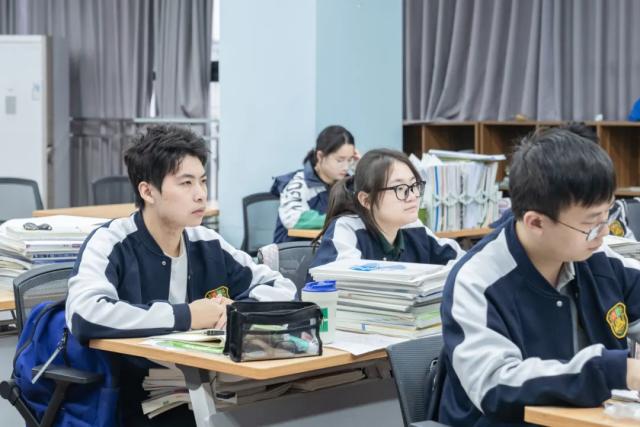 Students from Chongqing BI Academy sit and listen to a teacher in a classroom.