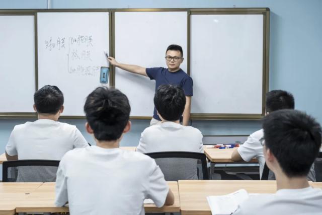 A teacher from Chongqing BI Academy explains a lesson to a student on a whiteboard.