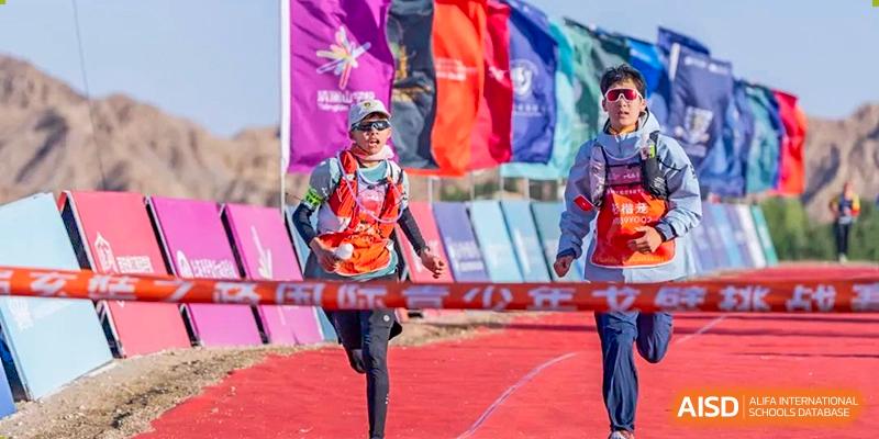 A runner from Chongqing BI Academy smiles as she runs past a finish line with colorful flags.