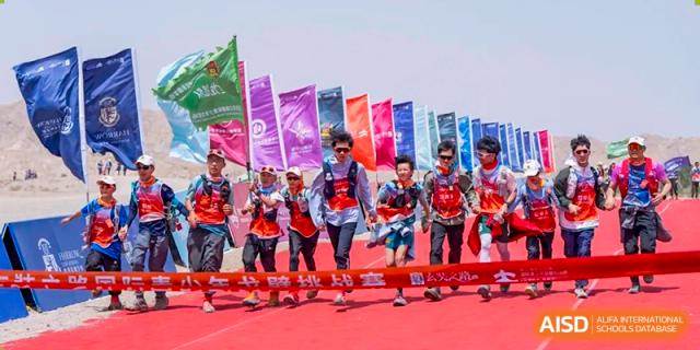 A group of male students from Chongqing BI Academy competes in a running race with colorful flags in the background.