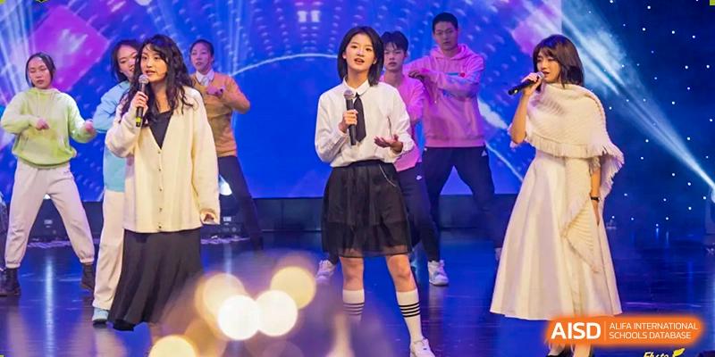 A young female student from Chongqing BI Academy sings and performs on a stage with a microphone in her hand.