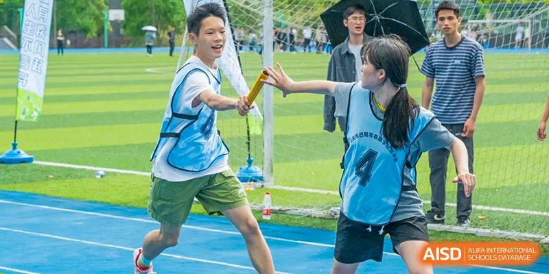 Students from Chongqing BI Academy pass a baton during a relay race on a sports field.