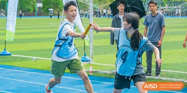 Students from Chongqing BI Academy pass a baton during a relay race on a sports field.
