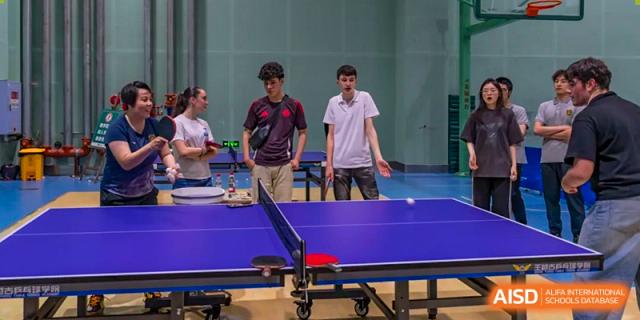 Students from Chongqing BI Academy play table tennis in an indoor sports hall.