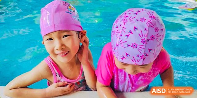 Two young girls from EtonHouse International School Nanjing wearing swim caps and smiling by a pool.