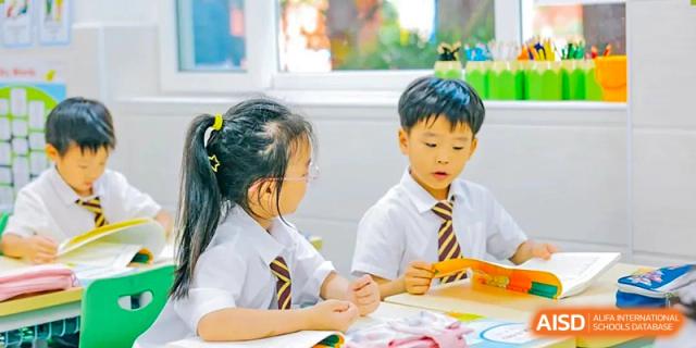Two young students from Shanghai Concord Bilingual School are sitting at a desk and working together.
