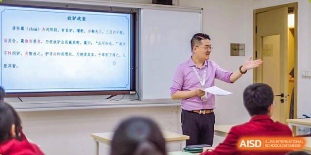 A teacher from Shanghai Concord Bilingual School stands in front of a whiteboard, giving a lecture to a class.